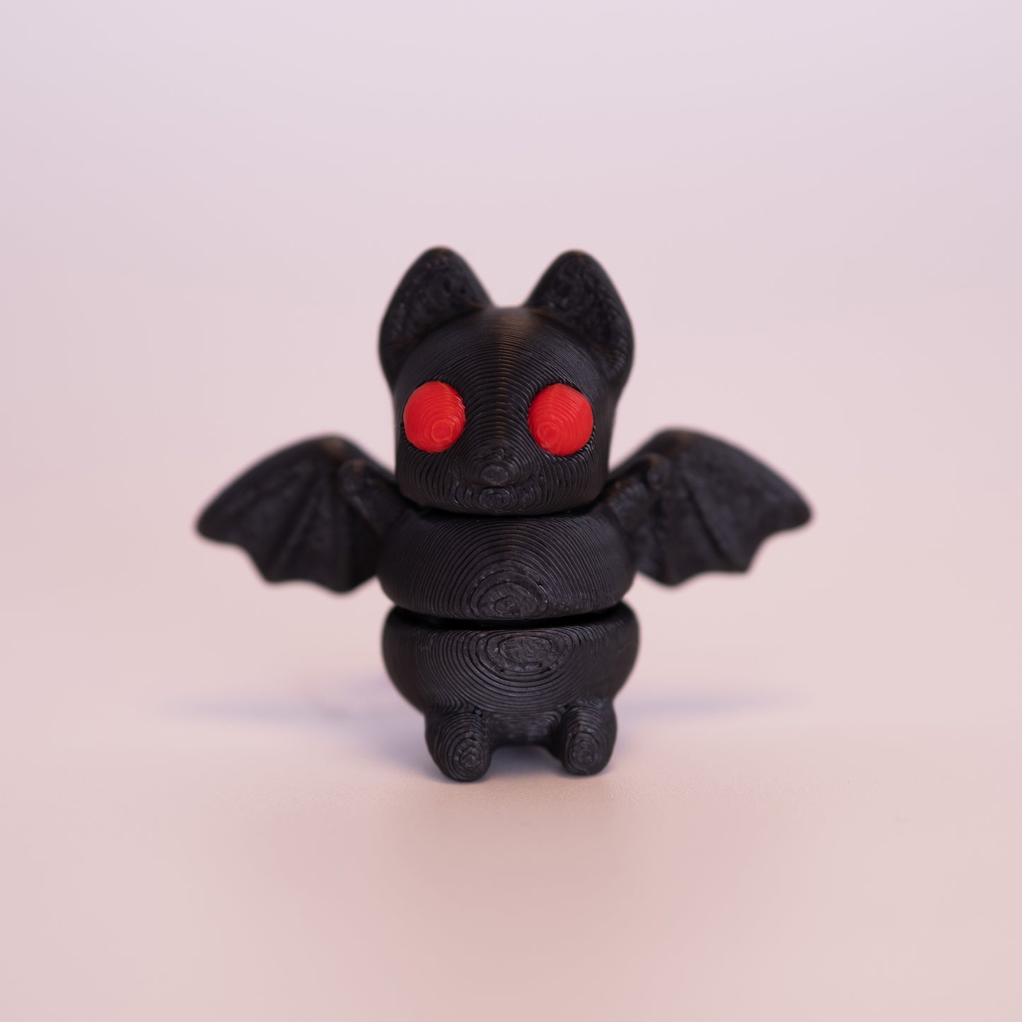 A 3D printed Bat figurine standing up on an off white background. The figurine is entirely black with round red eyes.