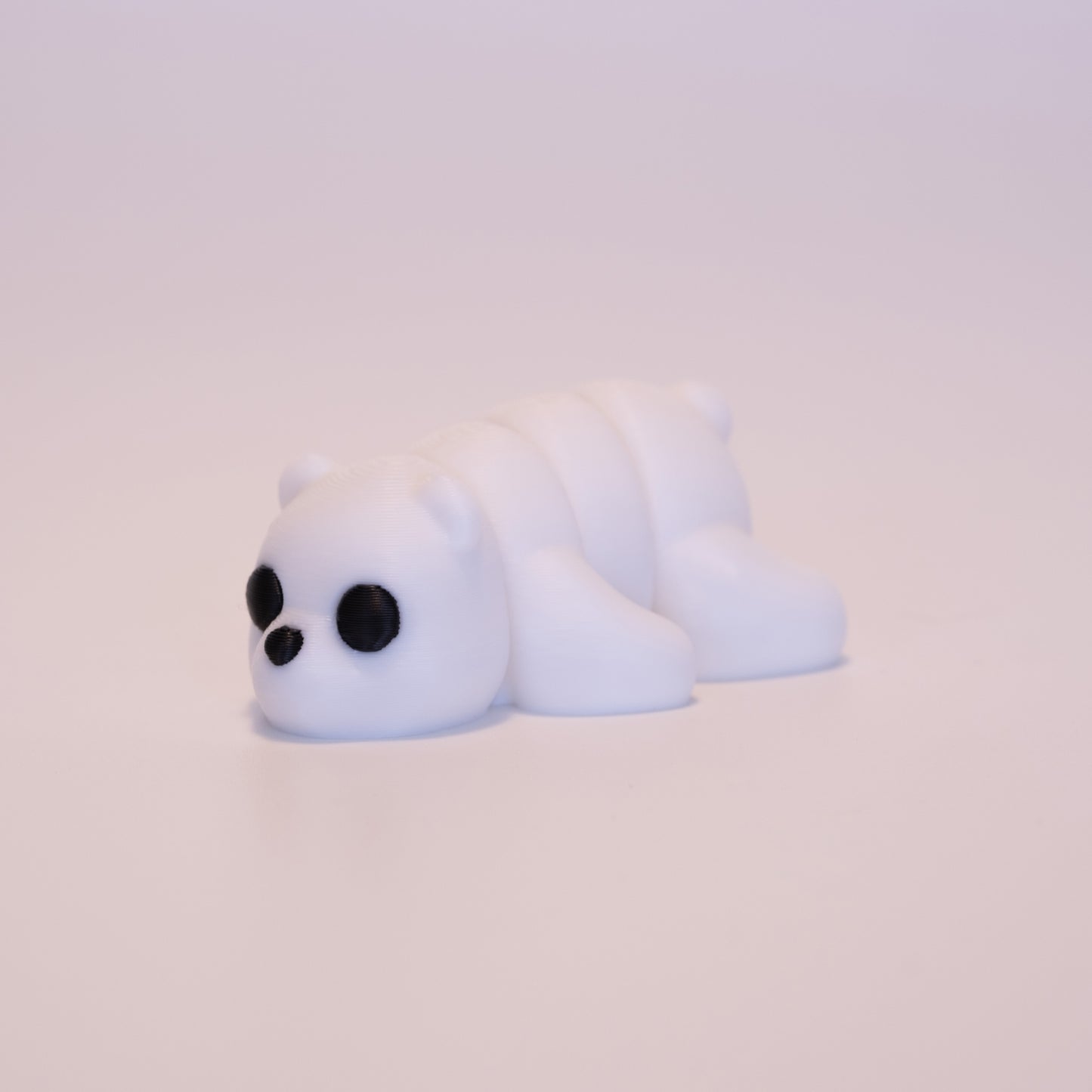 A 3D printed Polar Bear figurine laying on its stomach over an off white background. The figurine is entirely white with round black eyes and a black button nose.