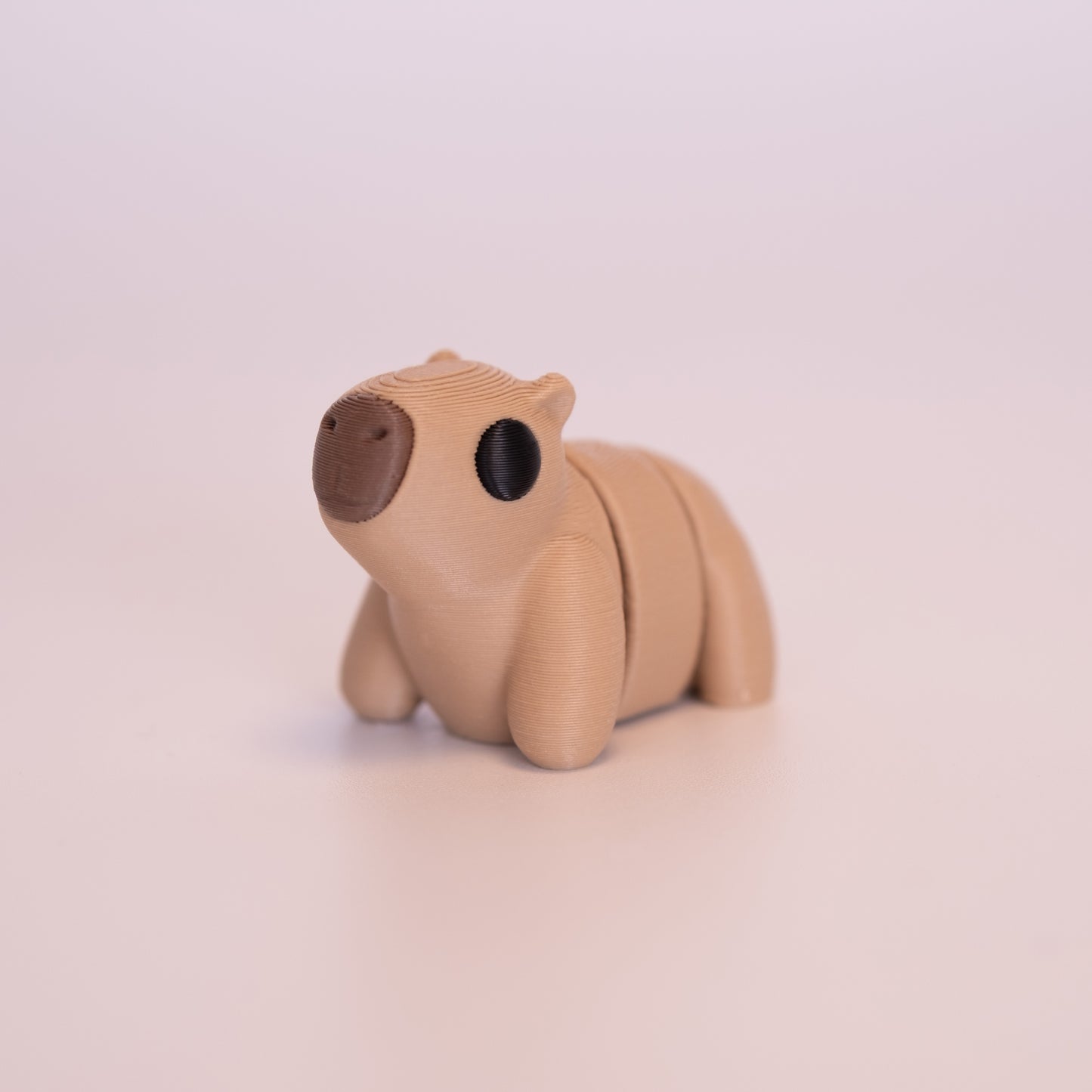 A 3D Printed Capybara figurine standing on its 4 legs on an off white background. The Capybara is mostly tan with round black eyes, and a brown nose.
