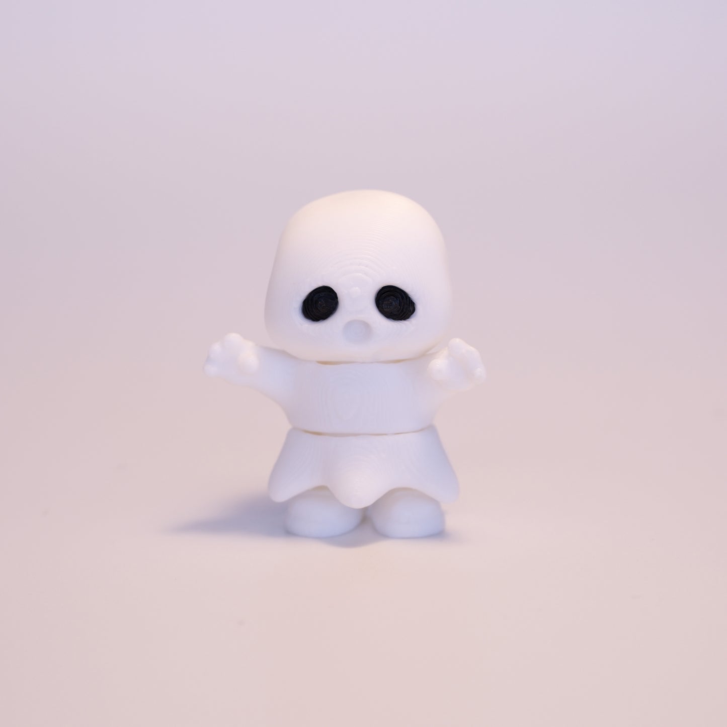 A 3D printed standing Ghost figurine with its hands up on an off white background. The Ghost is almost entirely white with an exception for black eyes.