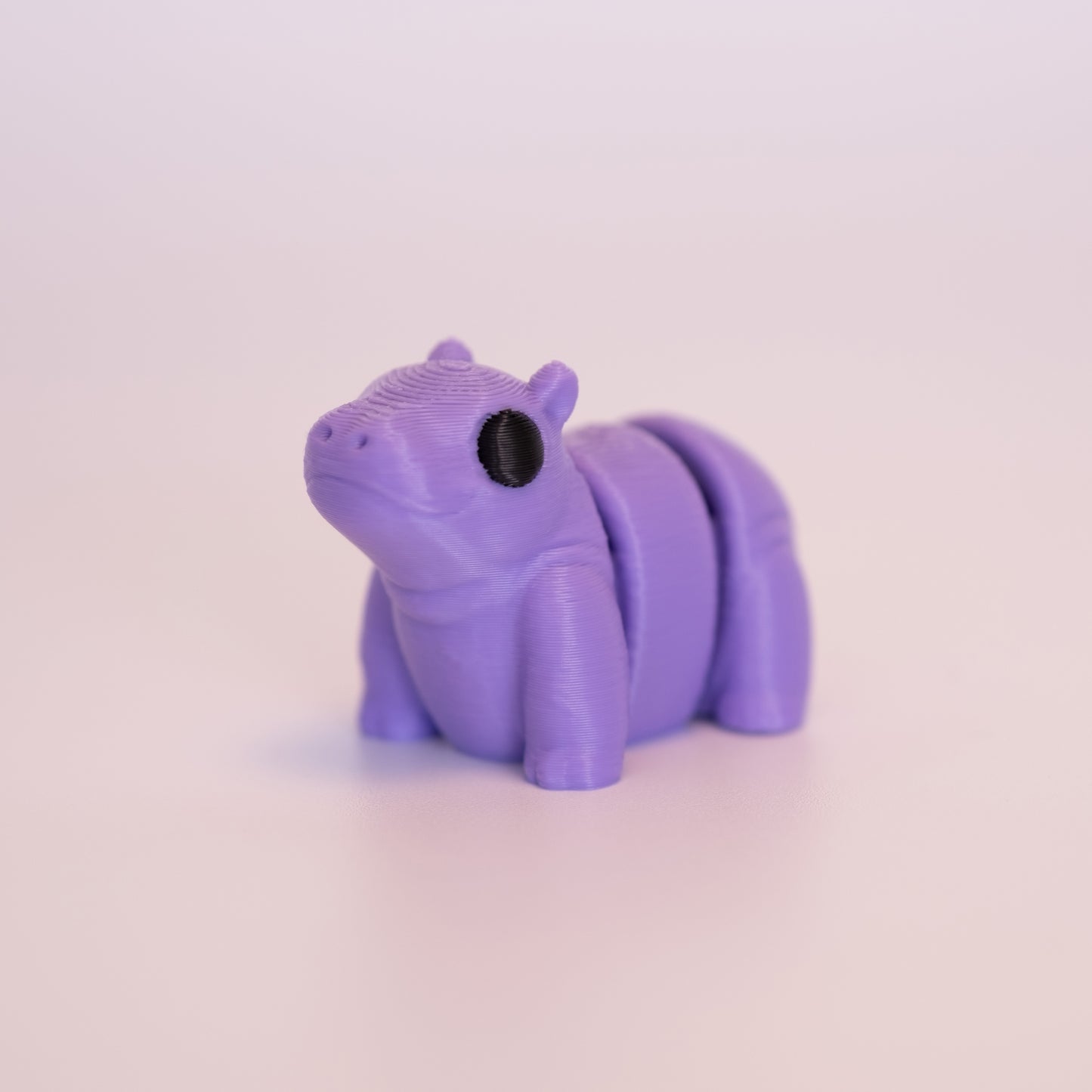 A 3D Printed Hippo figurine standing on its 4 legs on an off white background. The Hippo is almost entirely purple with round black eyes.