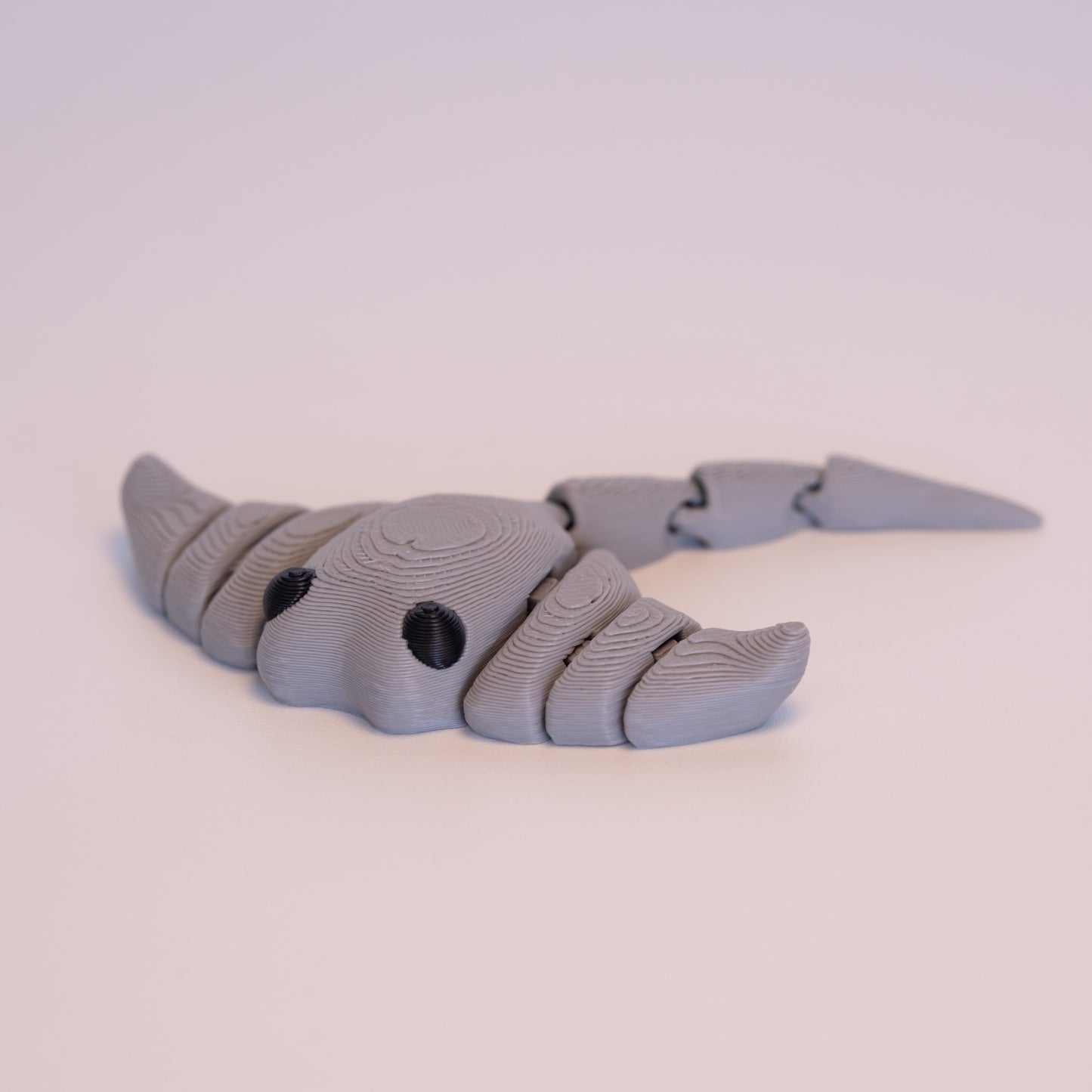 A 3D printed Manta Ray figurine laying flat on an off white background. The figurine is entirely light grey with round black eyes.
