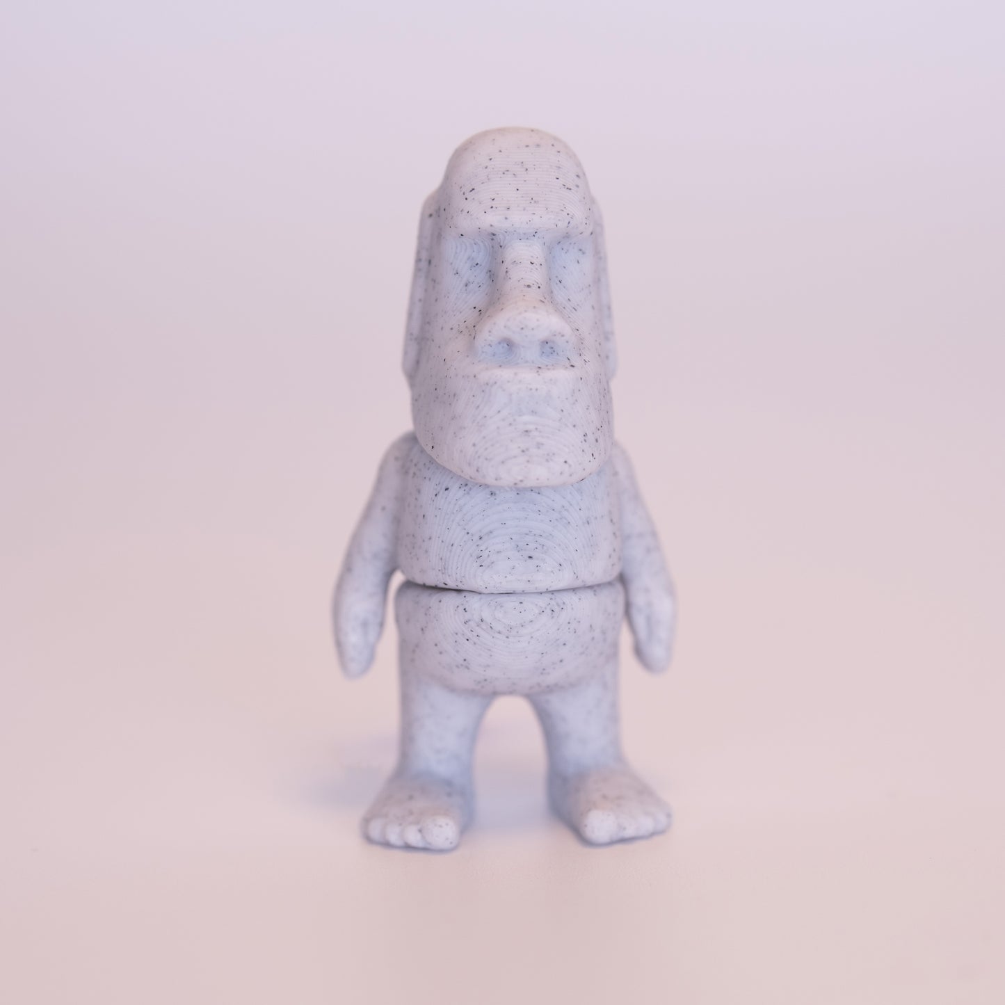 A 3D printed standing Angel figurine with her hands together praying. The Angel has beige skin, round black eyes, orange hair, a white dress and white wings on an off white background.