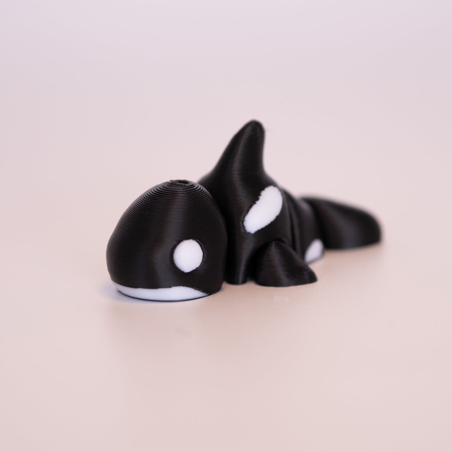 A 3D printed Orca figurine laying on its stomach over an off white background. The figurine is mostly black with round white eyes, and white accents.