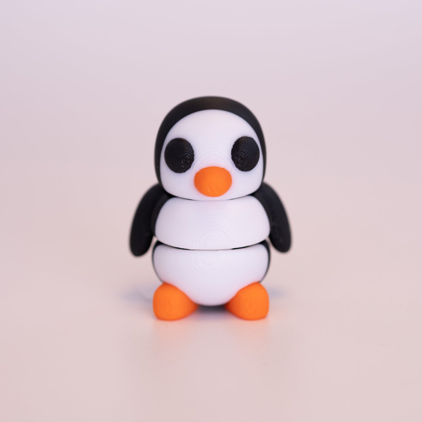 A 3D printed standing Penguin on an off white background. The Penguin is mostly black, with white on the front of the face and body. It has round black eyes, and an orange beak and feet.