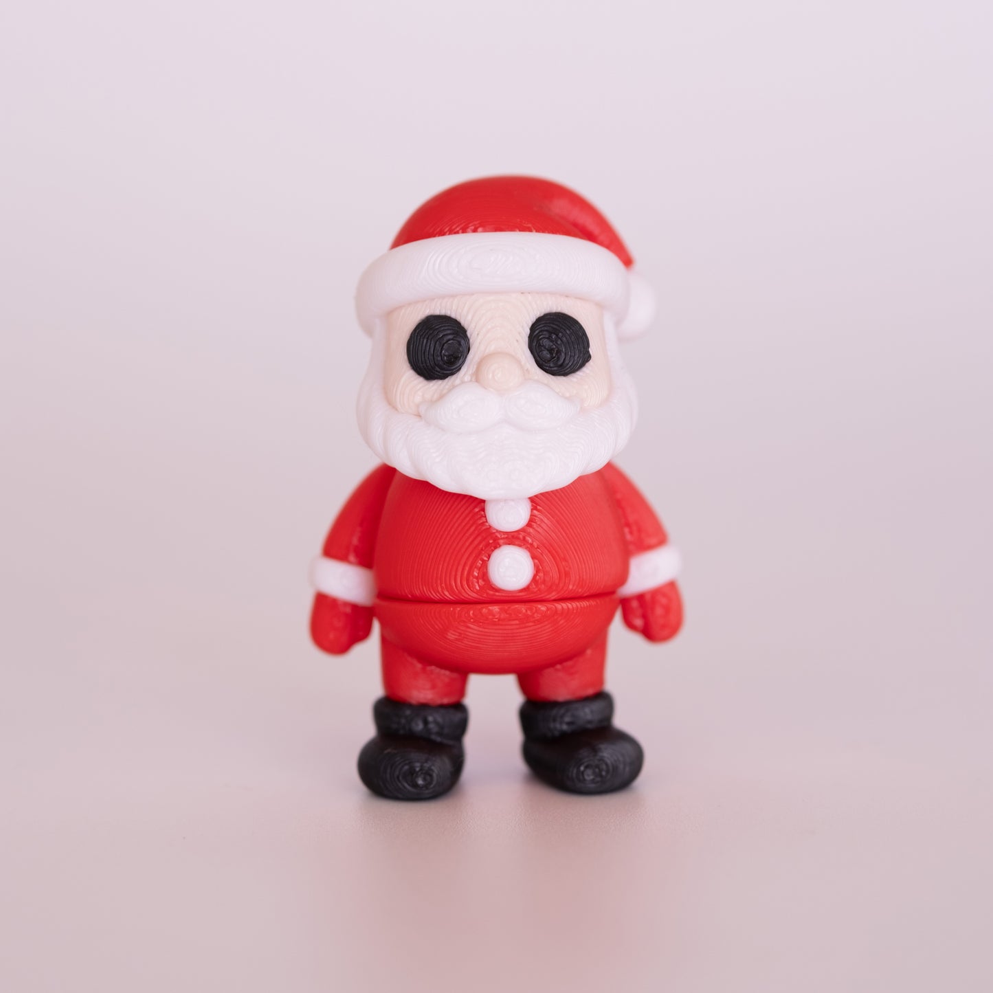 A 3D printed standing Santa figurine on an off white background. Santa has pale beige skin, round black eyes, and a white beard. He is wearing a mostly red outfit (including: a hat, button up shirt, pants, and gloves) with white accents and black boots.
