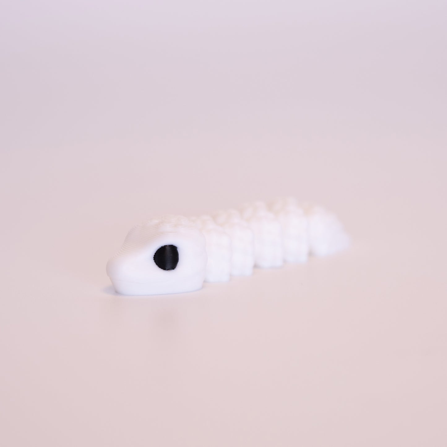 A 3D printed Snake figurine laying flat on an off white background. The figurine is entirely white with black eyes.