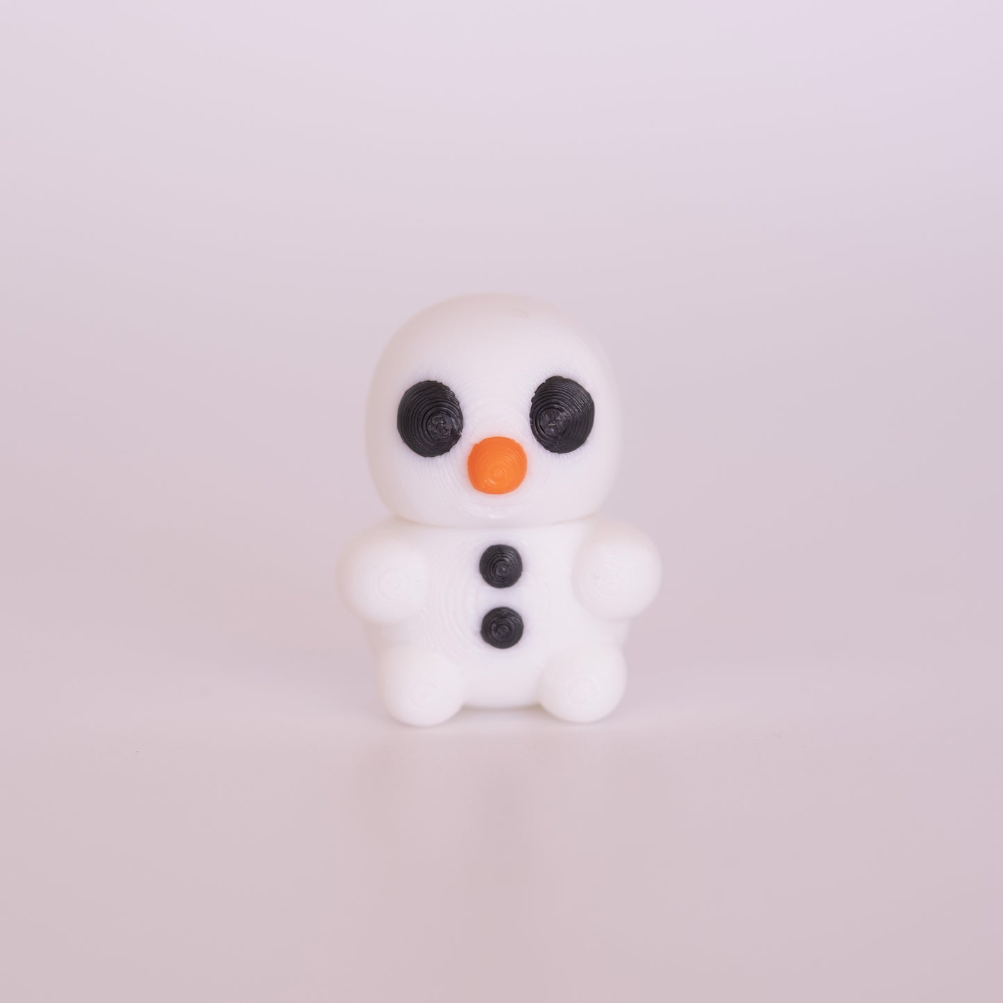 A 3D printed standing Snowman on an off white background. The Snowman is almost entirely white with round black eyes, an orange nose, and black buttons.