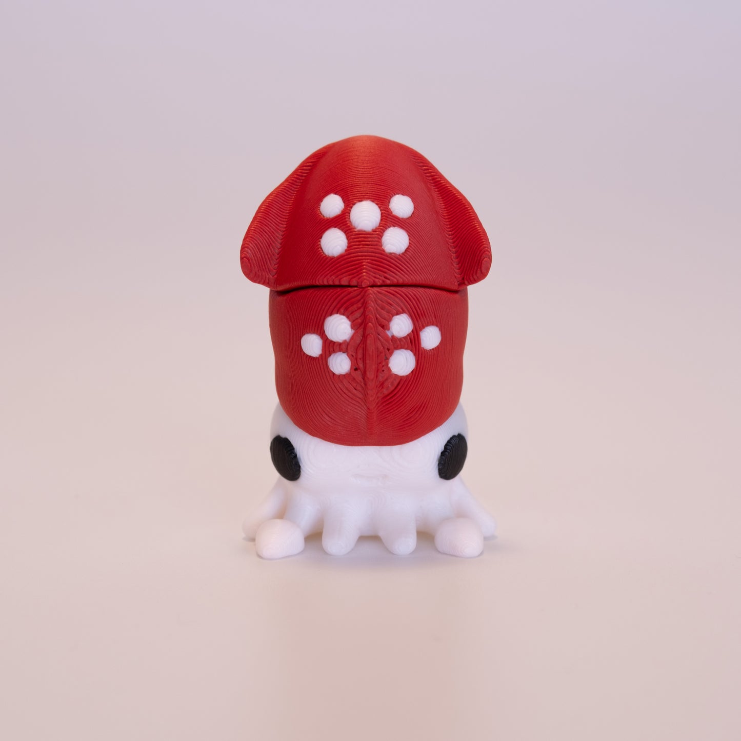 A 3D printed standing Angel figurine with her hands together praying. The Angel has beige skin, round black eyes, orange hair, a white dress and white wings on an off white background.