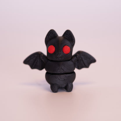 A 3D printed Bat figurine standing up on an off white background. The figurine is entirely black with round red eyes.