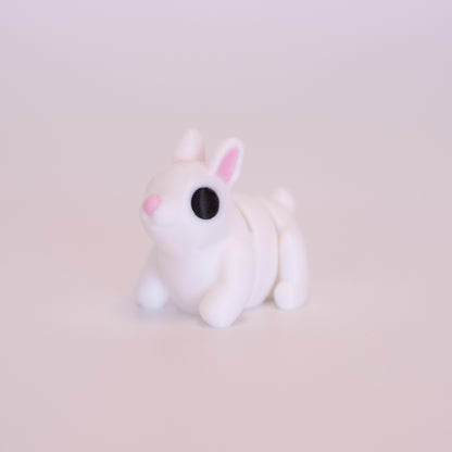 A 3D Printed Bunny figurine standing on its 4 legs on an off white background. The Bunny’s is mostly white with round black eyes, pink nose, and pink accents on the inner parts of its ears. 