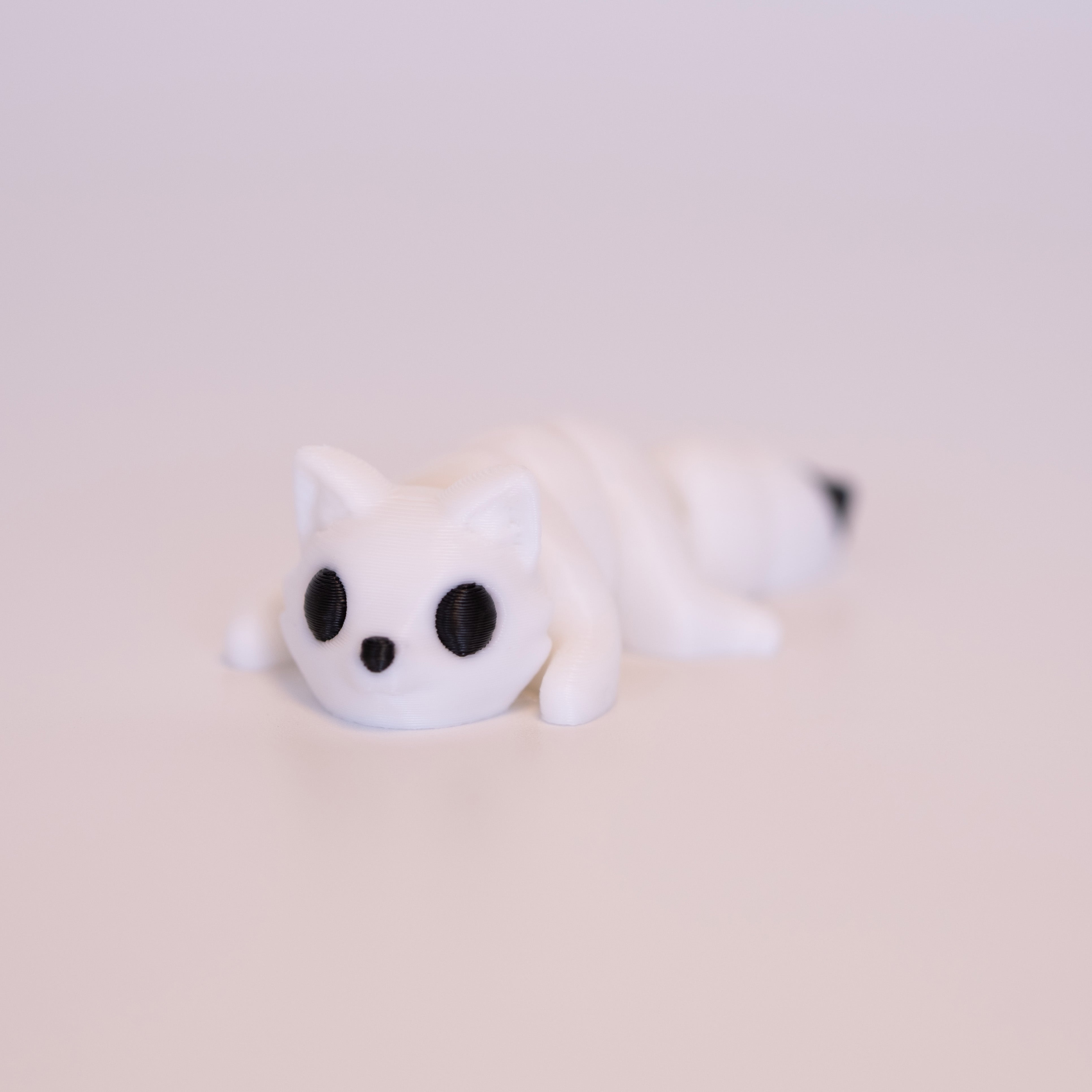 A 3D printed Arctic Fox figurine laying on its stomach over an off white background. The figurine is entirely white with round black eyes, a black button nose, and black accent on the tail.