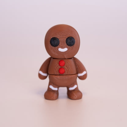 A 3D printed standing Gingerbread Man figurine on an off white background. The Gingerbread Man is a mostly warm brown, with round black eyes, red buttons, white smile, and additional white accents.