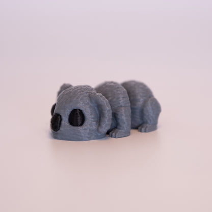 A 3D printed Koala figurine laying on its stomach over an off white background. The figurine is entirely grey with round black eyes and a black nose.