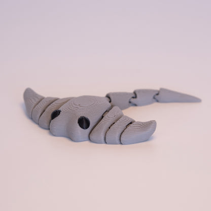 A 3D printed Manta Ray figurine laying flat on an off white background. The figurine is entirely light grey with round black eyes.