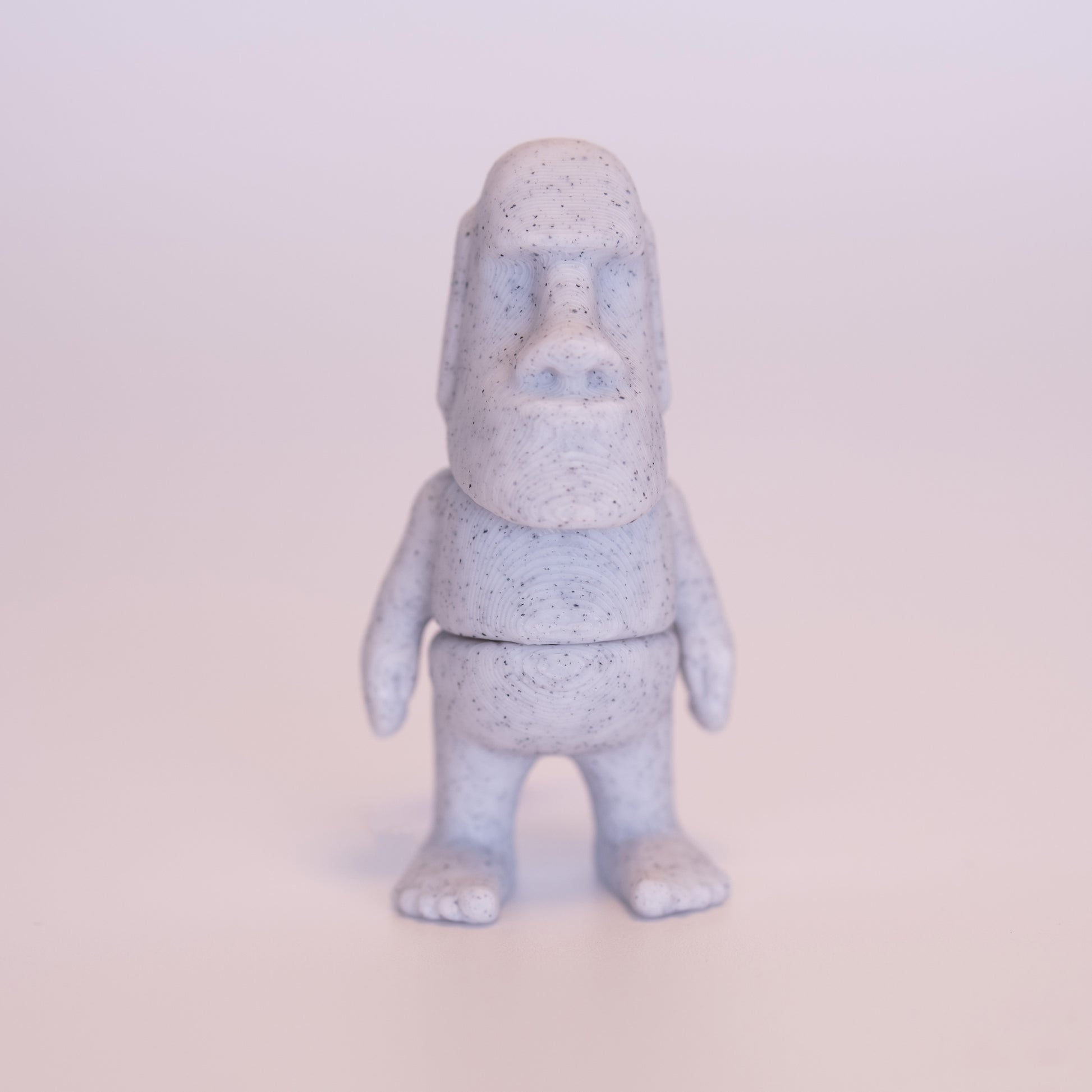 A 3D printed standing Angel  figurine with her hands together praying. The Angel has beige skin, round black eyes, orange hair, a white dress and white wings on an off white background.