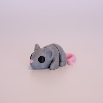 A 3D printed Mouse figurine laying on its stomach over an off white background. The figurine is mostly light grey with round black eyes, pink tail, and pink nose.