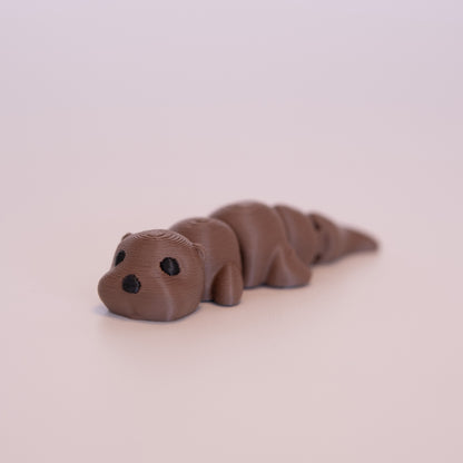 A 3D printed Otter figurine laying on its stomach over an off white background. The figurine is entirely brown with round black eyes and a black nose.
