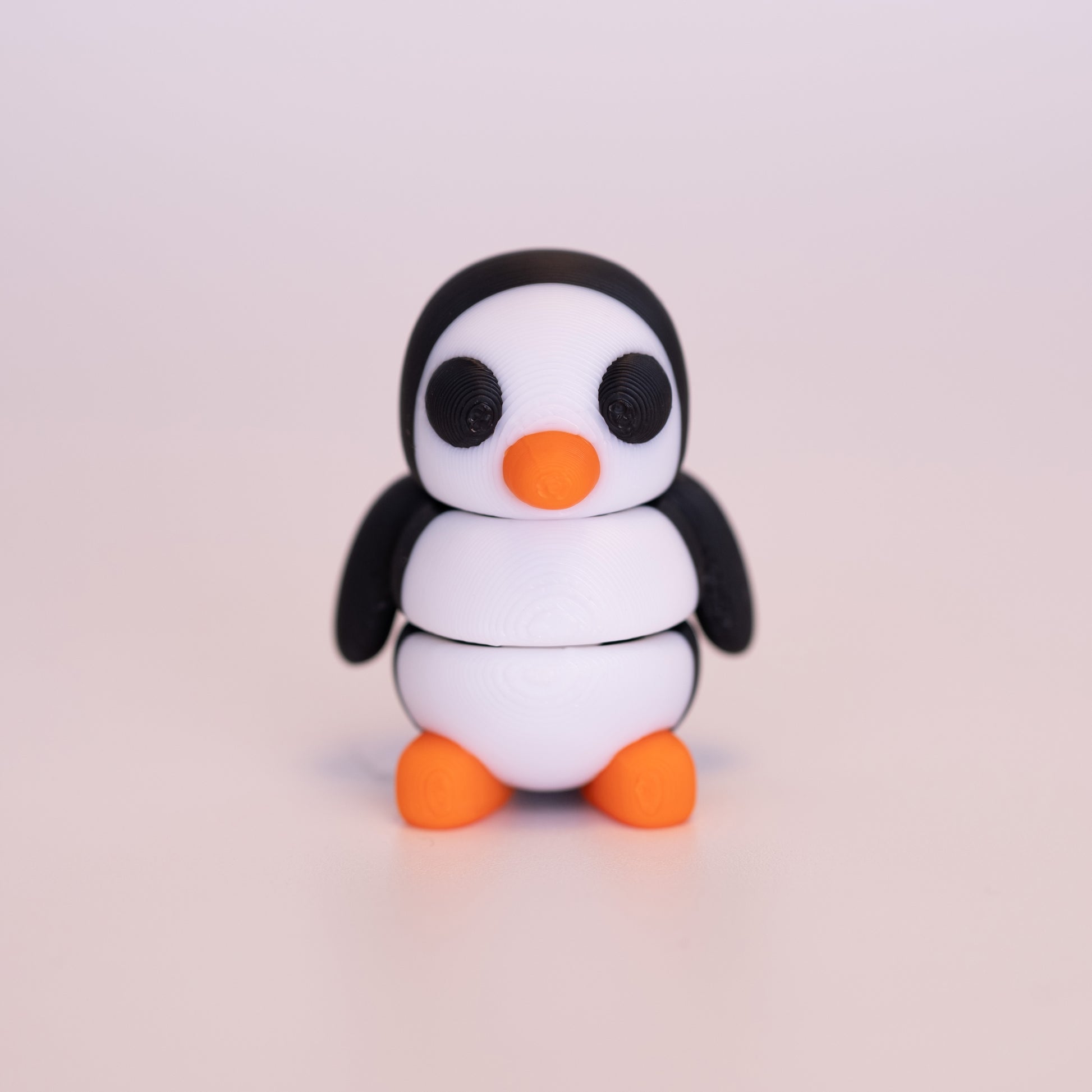 A 3D printed standing Penguin on an off white background. The Penguin is mostly black, with white on the front of the face and body. It has round black eyes, and an orange beak and feet.