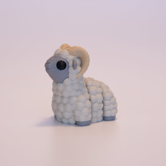 A 3D Printed Ram figurine standing on its 4 legs on an off white background. The Ram’s body is grey with muted beige wool, round black eyes, and tan horns. 