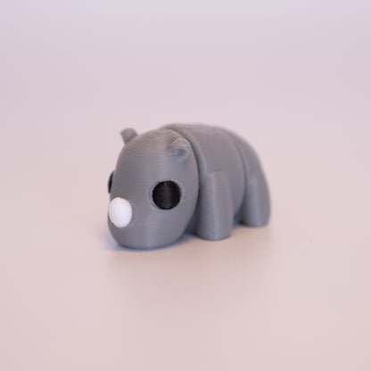 A 3D Printed Rhino figurine standing on its 4 legs on an off white background. The Rhino is mostly grey with round black eyes, and a white horn. 
