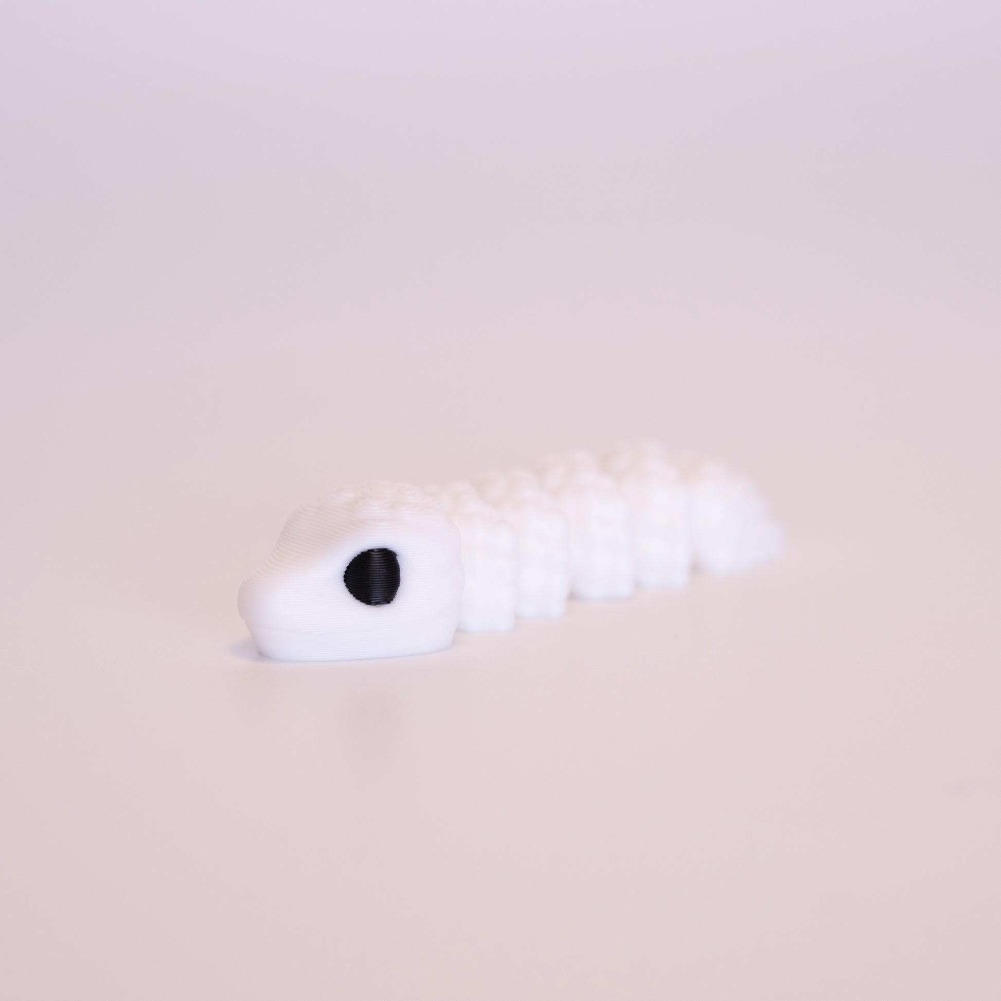 A 3D printed Snake figurine laying flat on an off white background. The figurine is entirely white with black eyes.