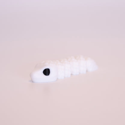 A 3D printed Snake figurine laying flat on an off white background. The figurine is entirely white with black eyes.