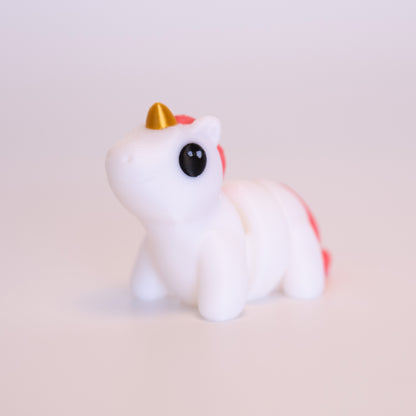 A 3D Printed Unicorn figurine standing on its 4 legs on an off white background. The Unicorn is mostly white, with a gold horn, pink mane and tail, and round black eyes with 2 small white accent dots in each eye.